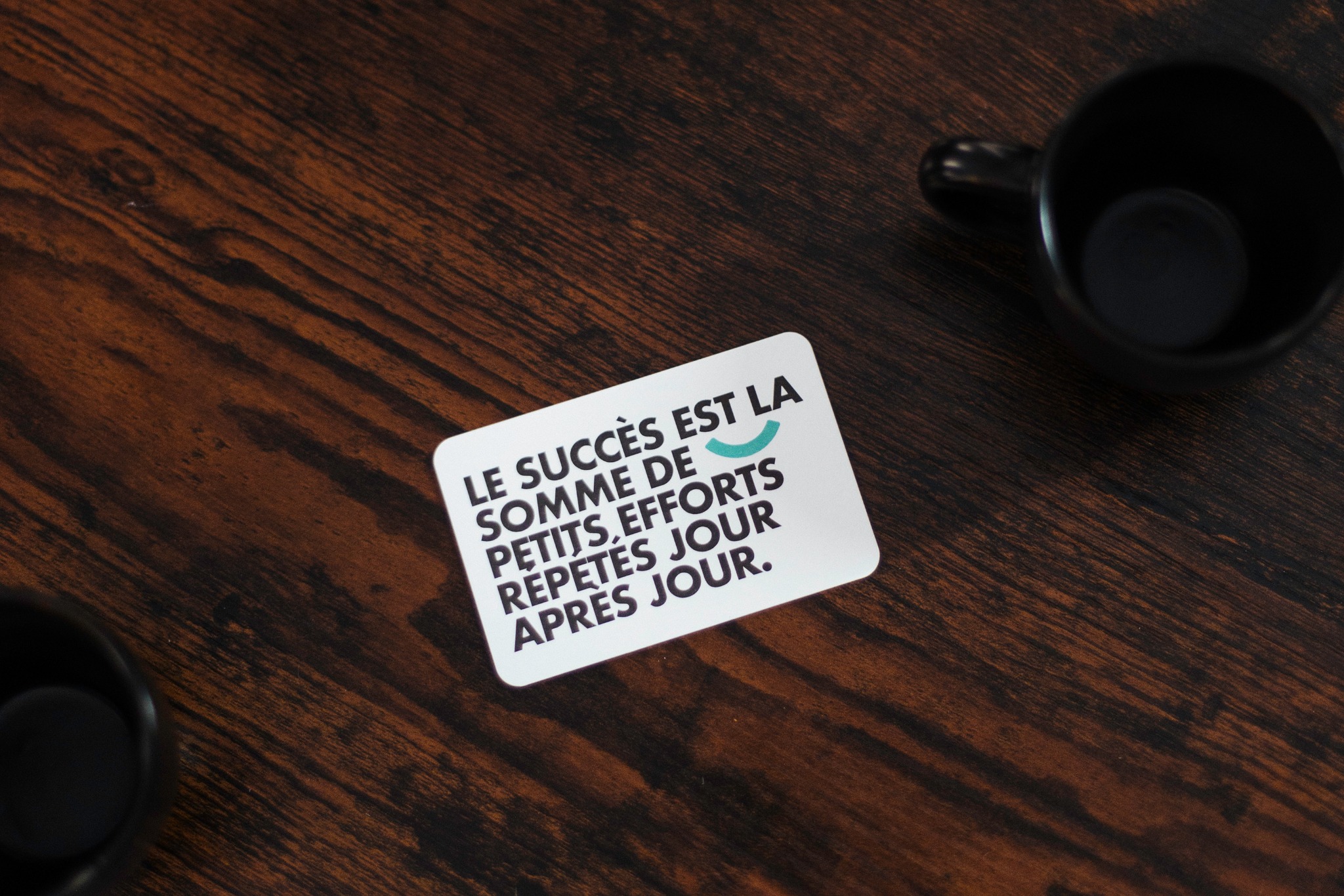 Carte Elitia posée sur une table en bois, entre deux tasses sombres.